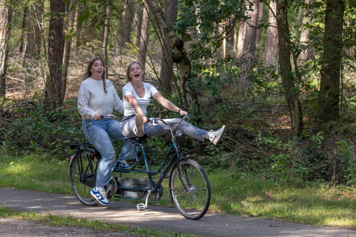 Twee vrouwen lachend op een tandem in het bos
