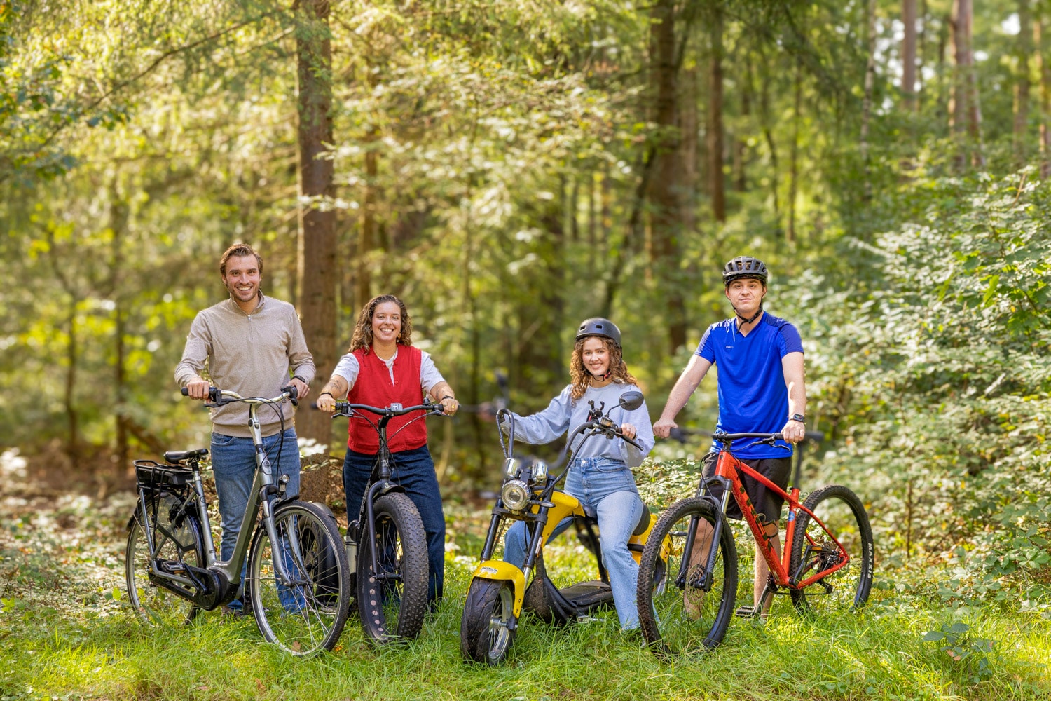 Groep vrienden met verschillende fietsen en e-voertuigen in het bos bij Outdoor Harderwijk