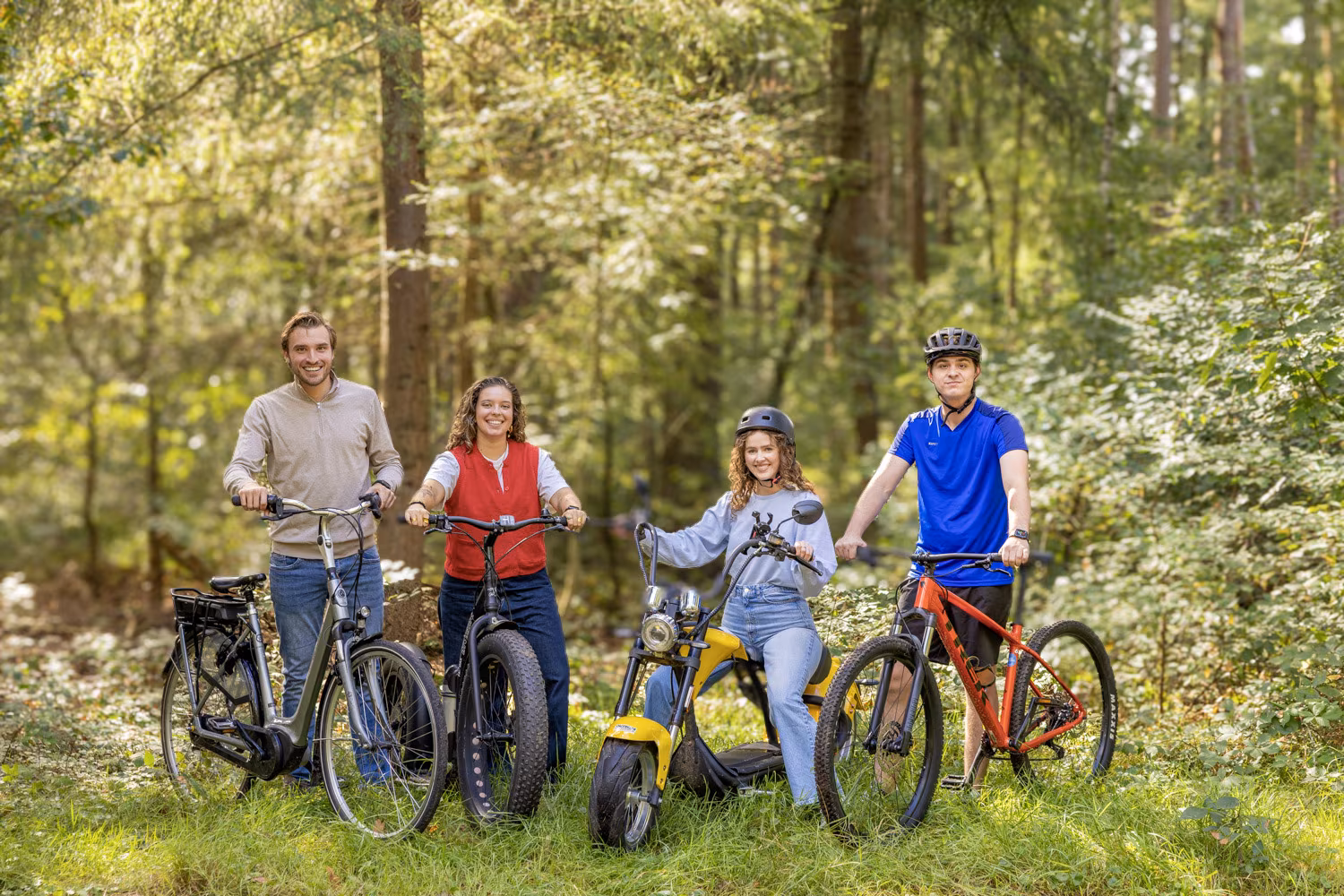 Groep vrienden met verschillende fietsen en e-voertuigen in het bos bij Outdoor Harderwijk