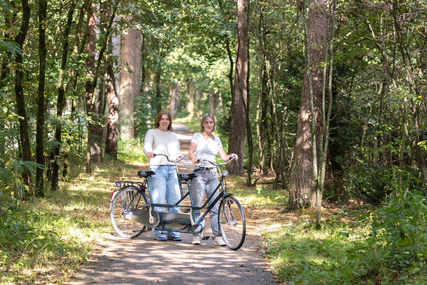 Twee dames poseren op een tandem in het bos